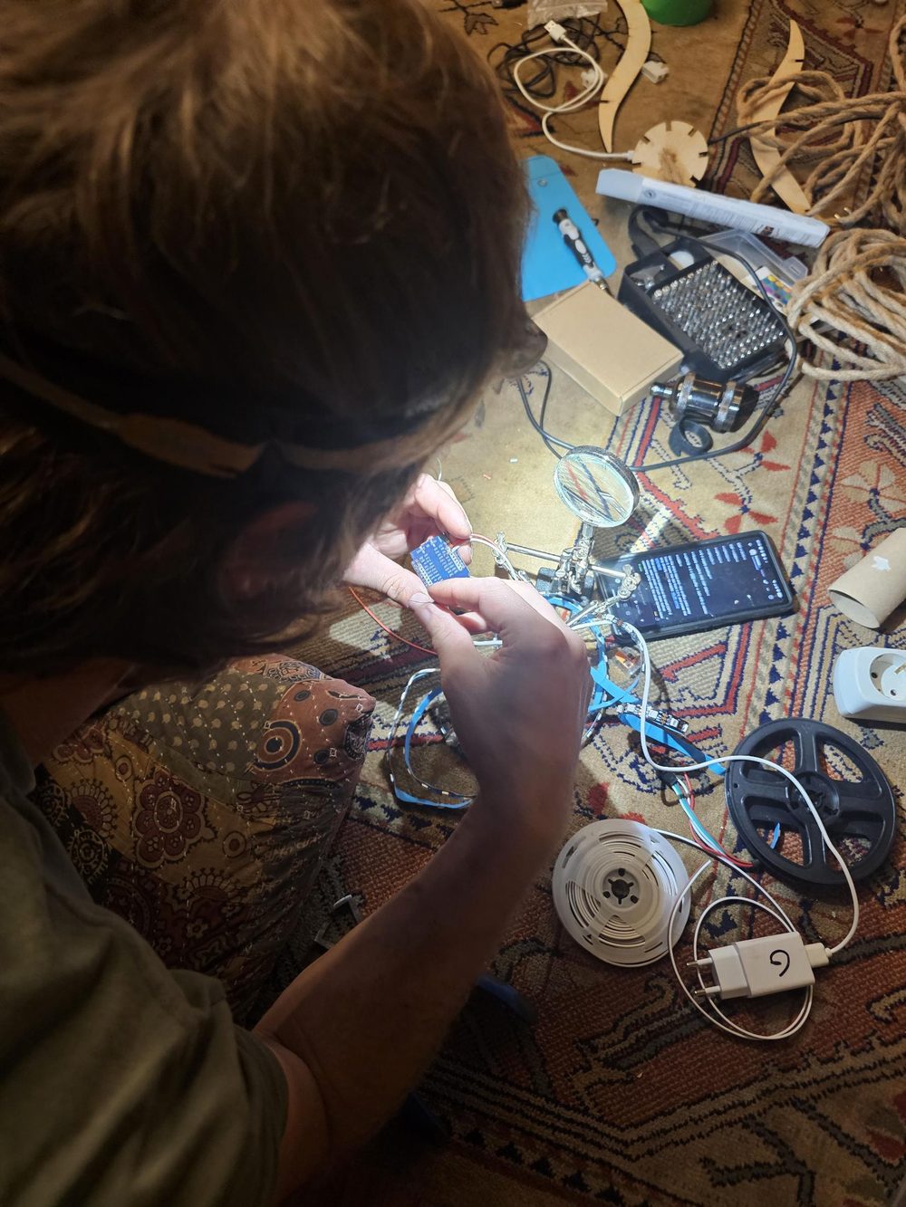 Soldering an ESP32 board to an LED strip, with laser-cut lamp parts and rope in the background