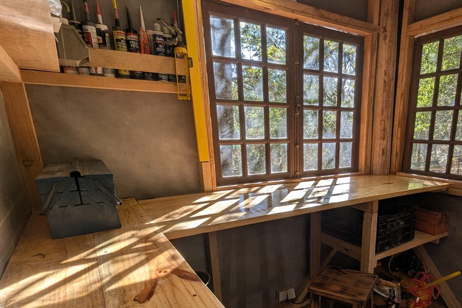 The workshop: an L-shaped timber bench under multi-paned windows looking into the trees